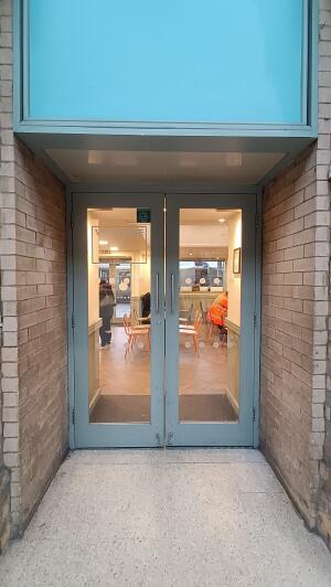 Light blue metal-framed glass doors to venue. Pull from handles at centre to open.
