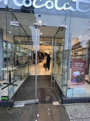 Glass doors with metal handles at centre. Push from handles to open. Ramp up at foot of doors.