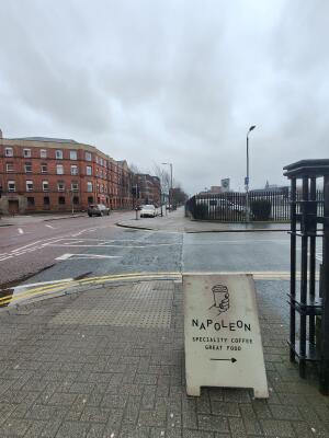 From entrance facing left. A-frame sign on pavement in foreground. Sign points right to venue.