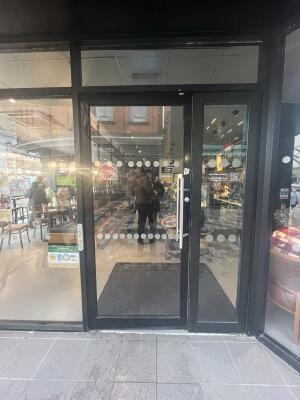 Black metal-framed glass door. Push from handle on right to open. Button for assistance on left of door.