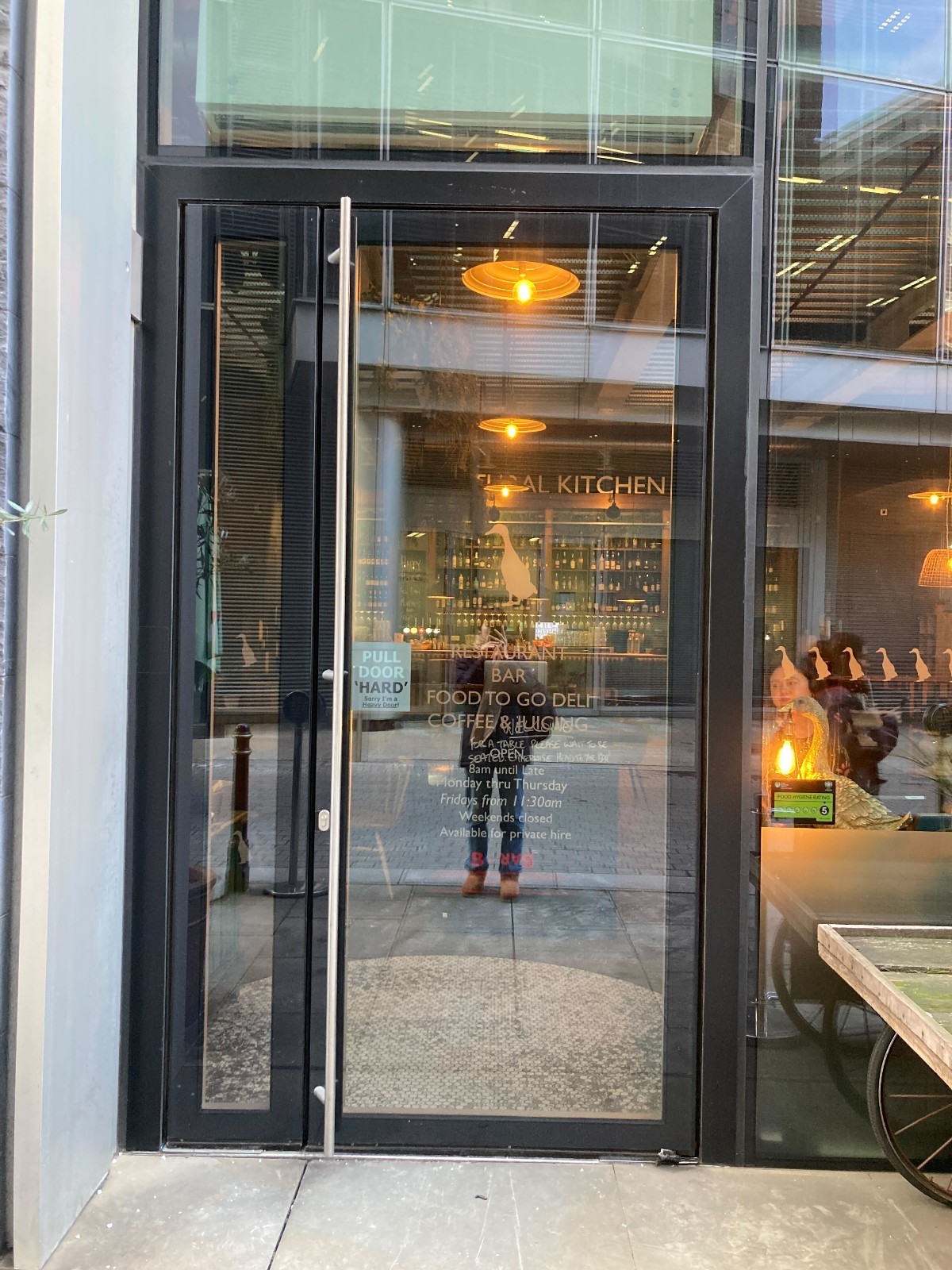 From after restaurant barriers facing straight. Black framed glass door ahead. Pull silver metal handle on left to open.
