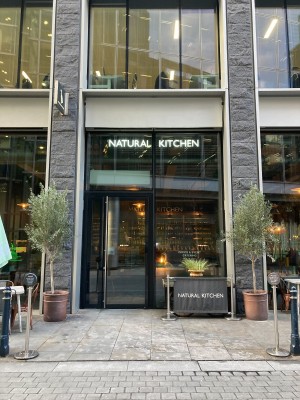 Facing venue. Restaurant barriers on left and right. Path ahead to entrance at back left.
