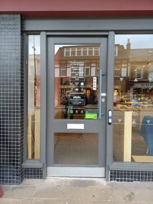 Grey metal-framed glass door. Push from handle on right to open. Button for assistance on right.