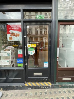 Black glass door with handle at left, push to open. Assistance bell at left of door.