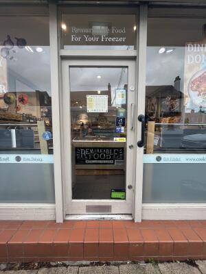 Light grey wood-framed glass door. Push from metal handle on right to open. One step up before door.