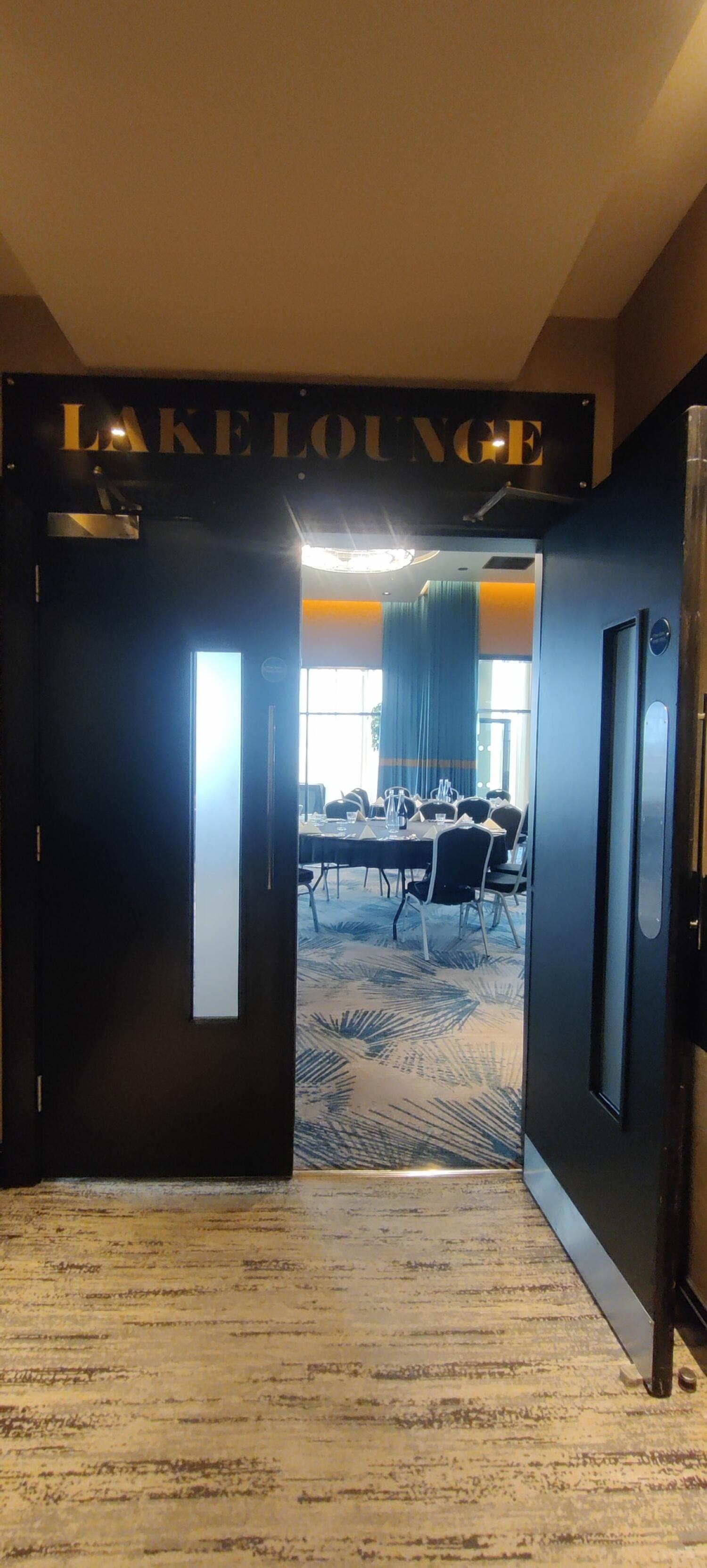 From end of corridor facing right. Third set of black doors with narrow vertical glass panels ahead. Pull from handles at centre to open.