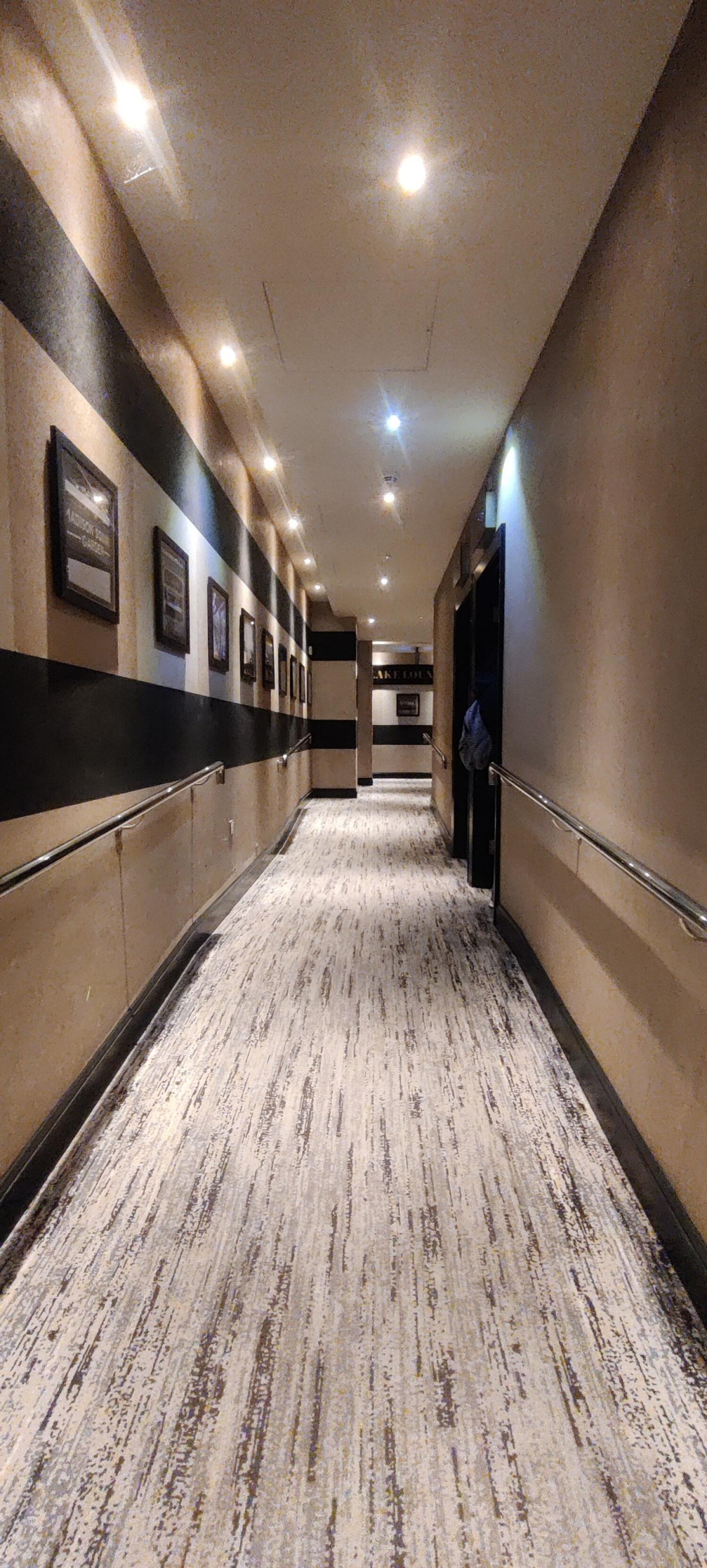 From second archway facing straight. Ramp up path ahead through corridor with handrails along right and  left walls.