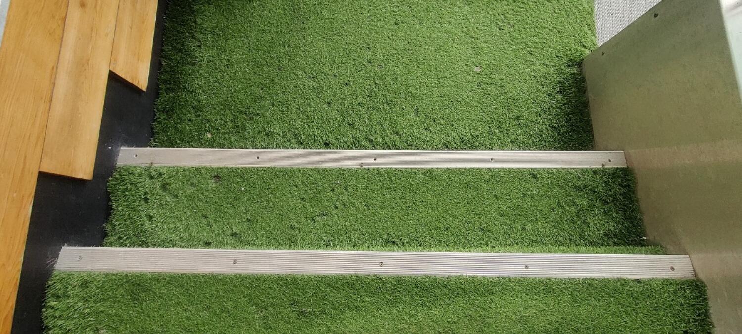 Two steps down ahead with green turf covering. Metal strips along step edges.