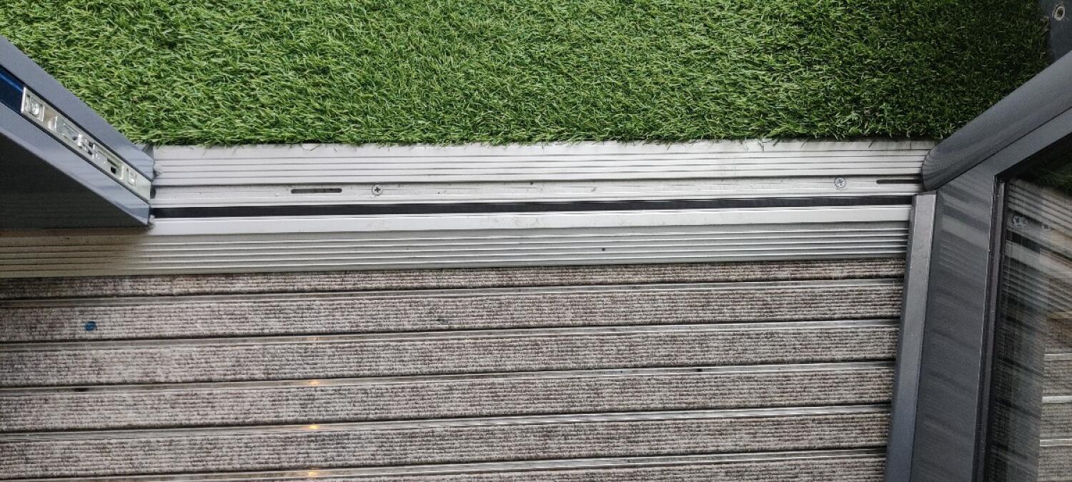 Small bump at foot of door. Artificial grass outside threshold.