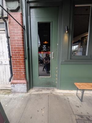 Dark green wooden door with central glass panel. Push from metal handle on right to open.