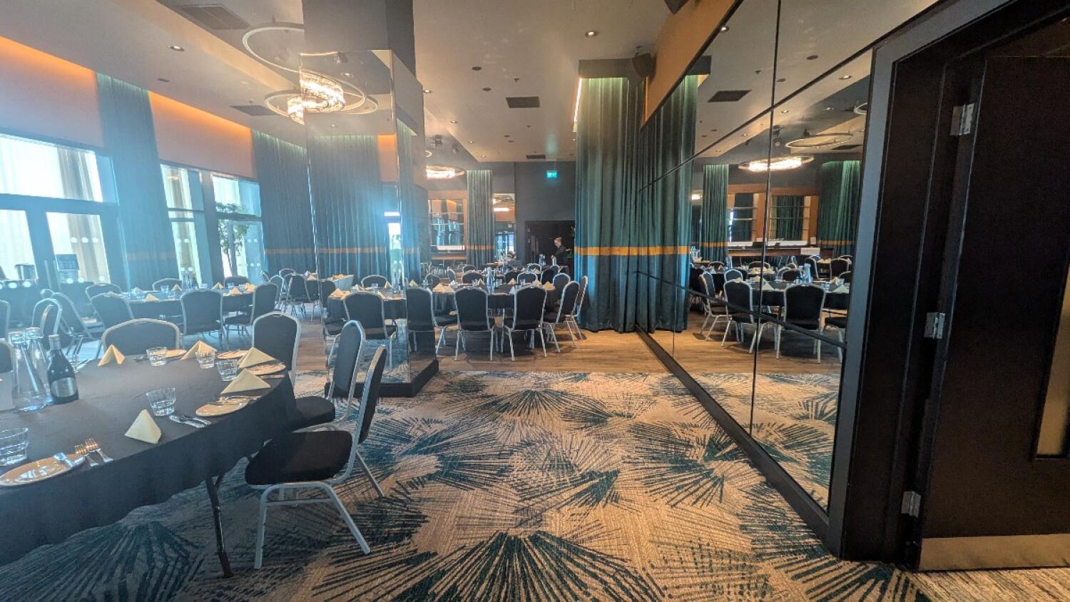 From entrance facing right. Tables with chairs along left. Pillar covered with glass on back left. Additional tables and chairs to right.