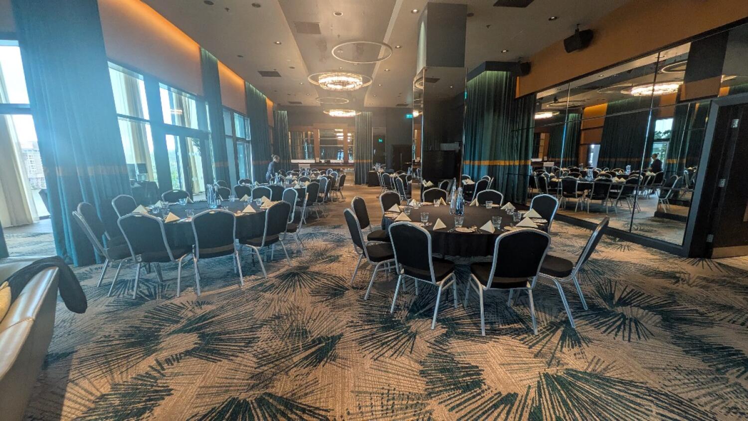 From couch facing right. Round tables with chairs arranged across space. Pillar back right. Bar counter visible at back.