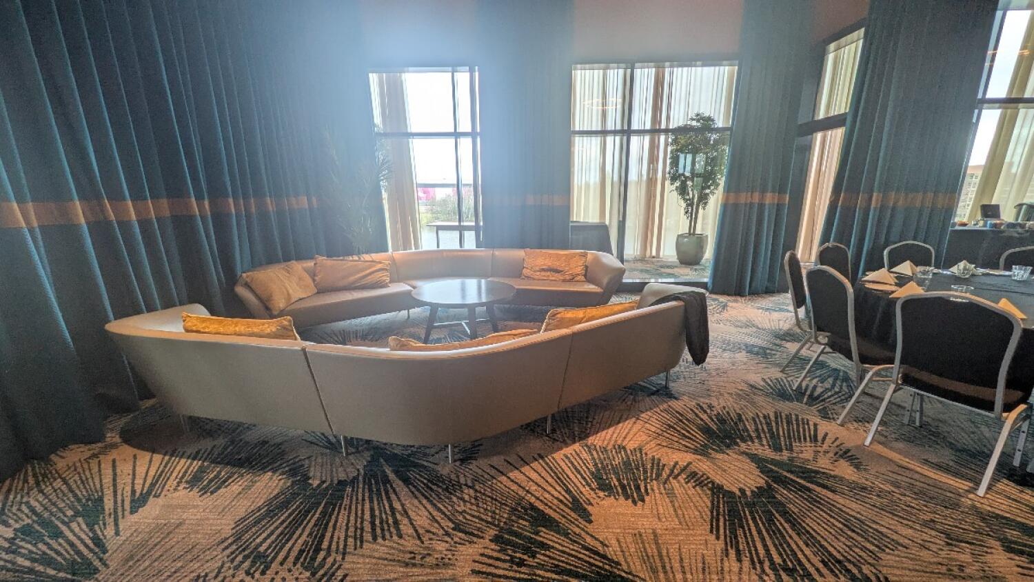 From left of round table and chairs facing straight. Couch with cushions in ahead. Round table in middle of sofa. Dining chairs and tables to right.