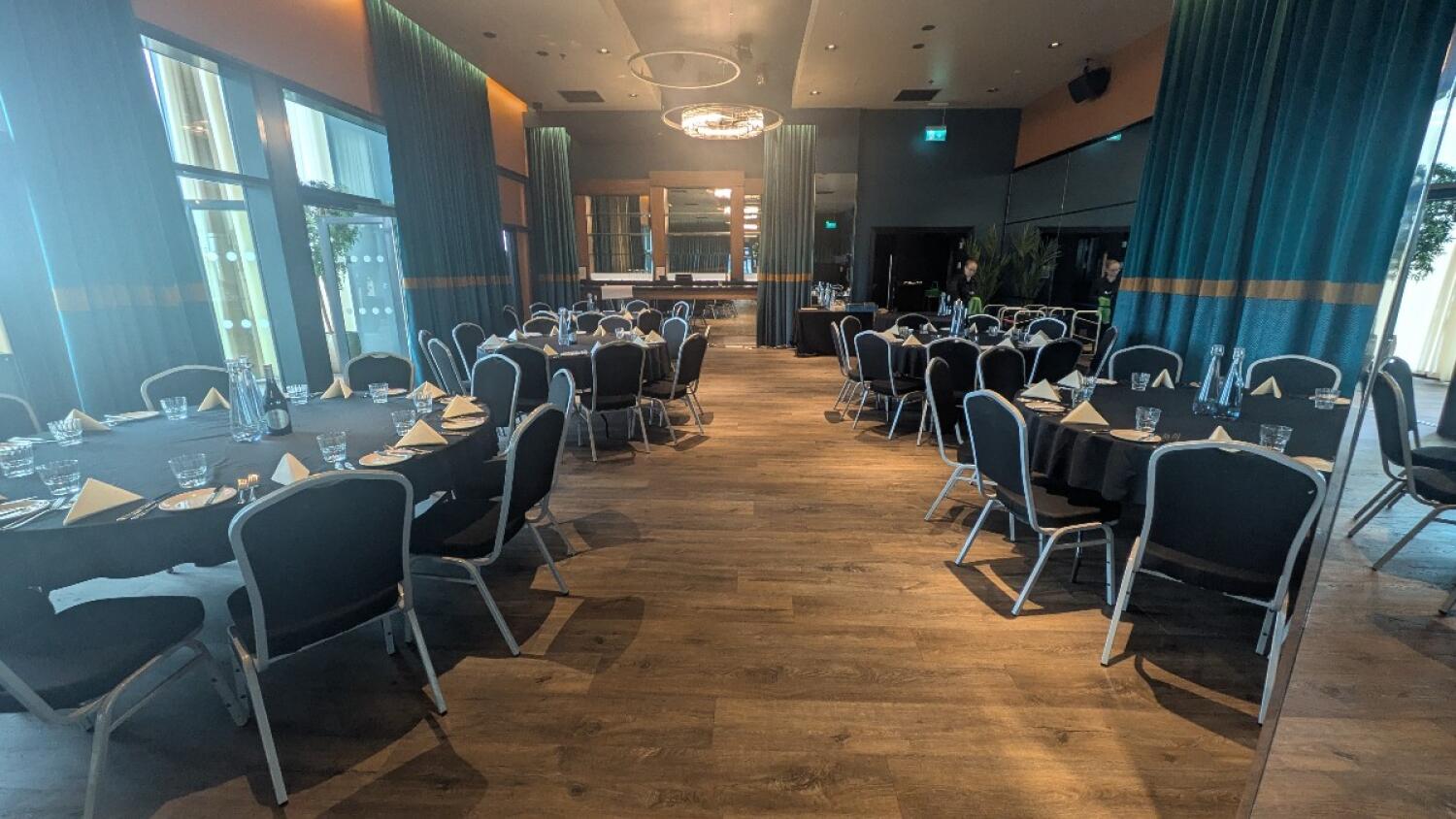 From pillar facing straight. Round tables with chairs along left and right. Path to back space in centre. Additional tables and chairs at back.