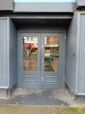 Dark grey wood-framed glass doors ahead. Pull from metal handles at centre to open.