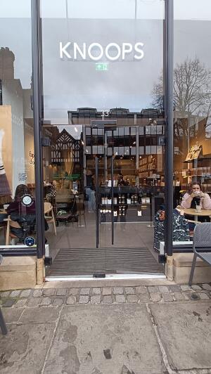 Glass doors with vertical black metal handles to venue. Push from handles at centre to open.