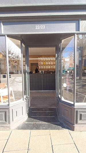 Black framed glass panelled door to venue. Push handle on left to open.