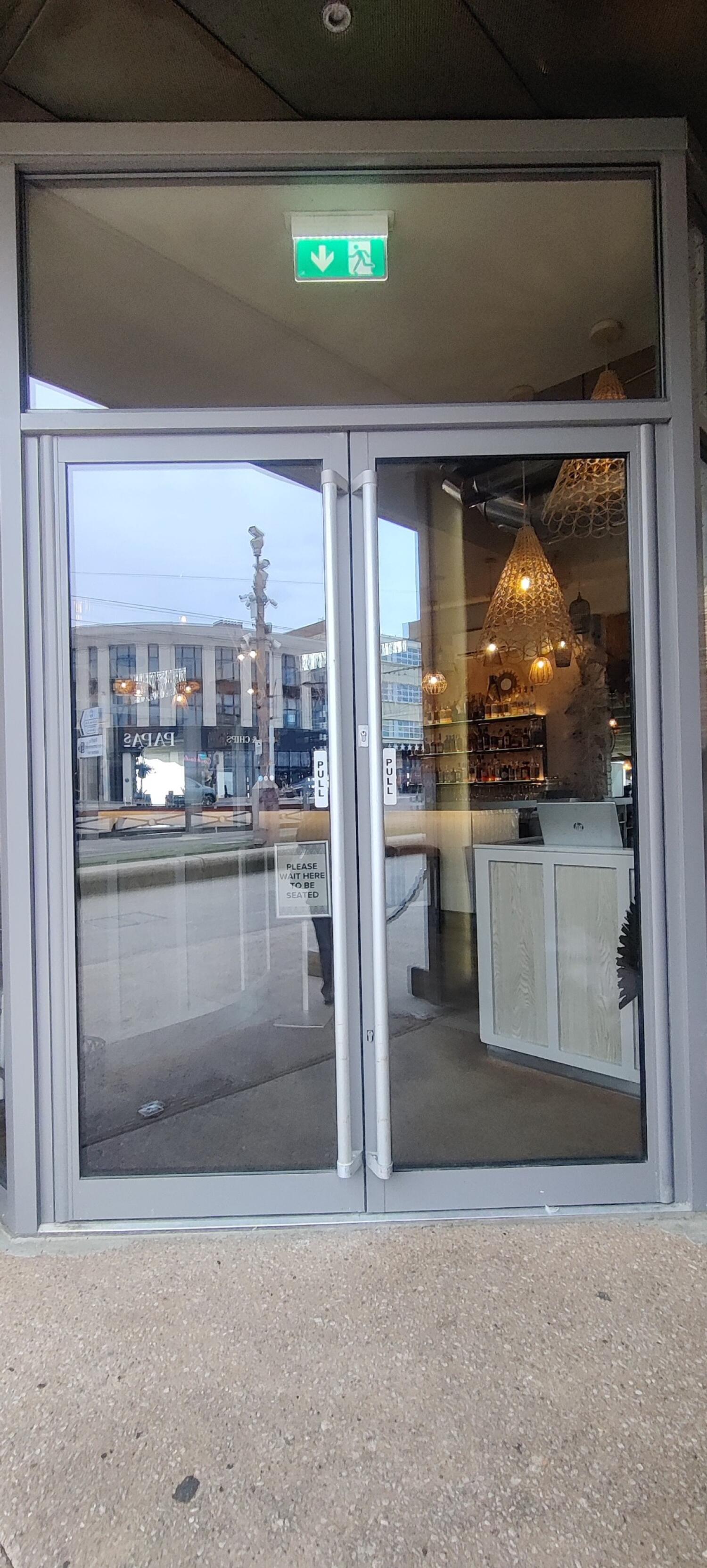 From archway facing left. Grey metal-framed glass doors. Pull from handles at centre to open.