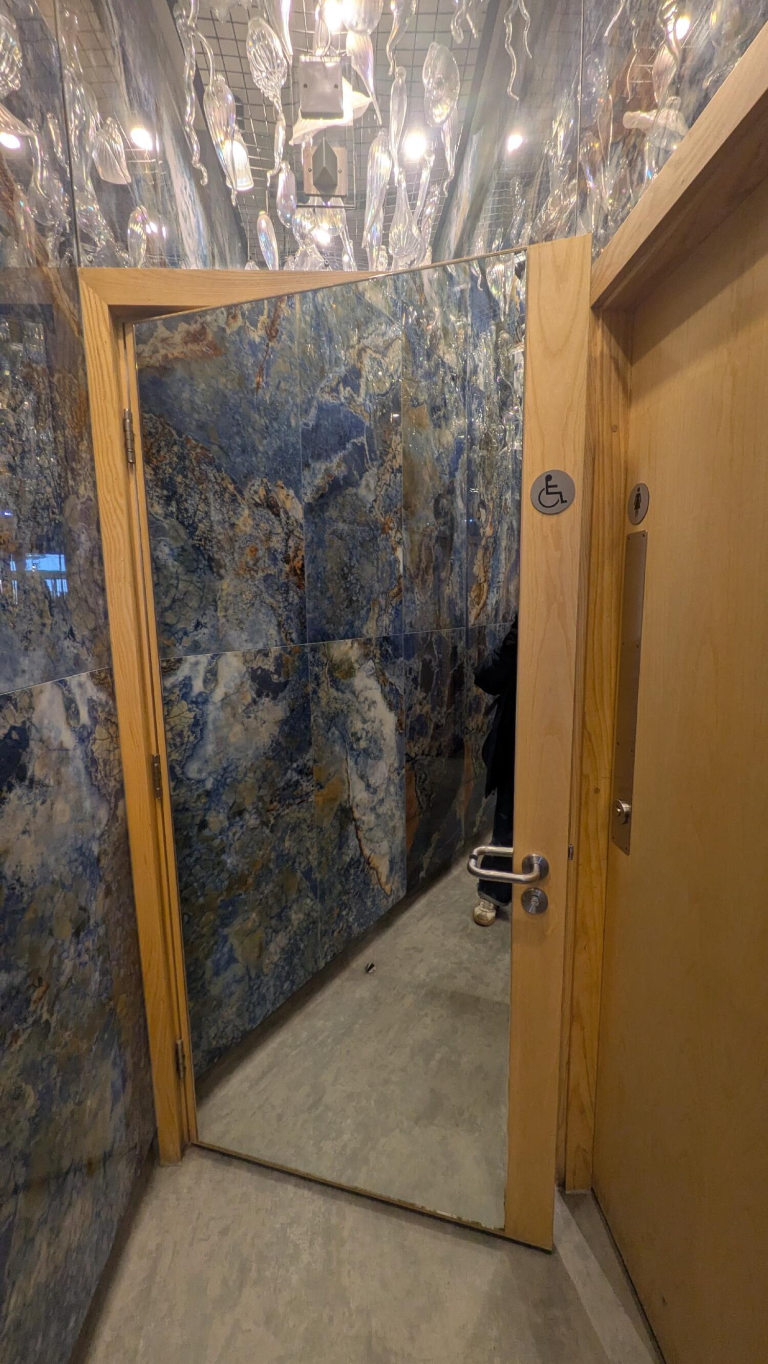 From end of path facing straight. Light wood door with metal handle on right. Pull from handle on right to open.