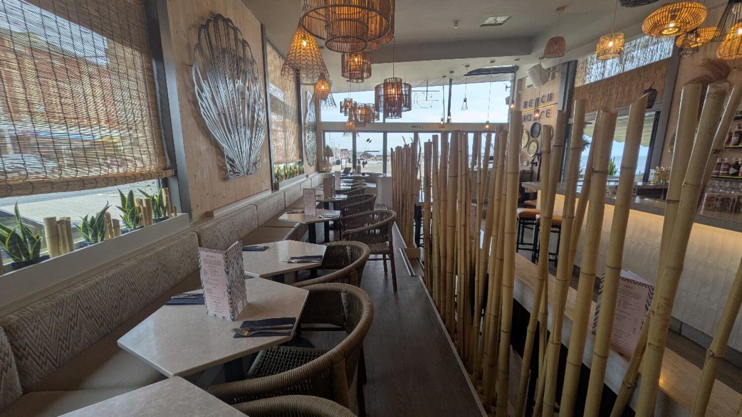 From top of steps facing right. Half booth along left wall. Tables and chairs in centre. Bar counter with stools along right behind fencing.