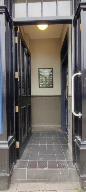 Black wooden framed metal door ahead. Push strip in right to open. Grab rail along right.