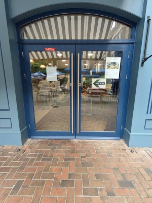 Glass door with blue frame ahead. Push silver metal handles in centre to open.