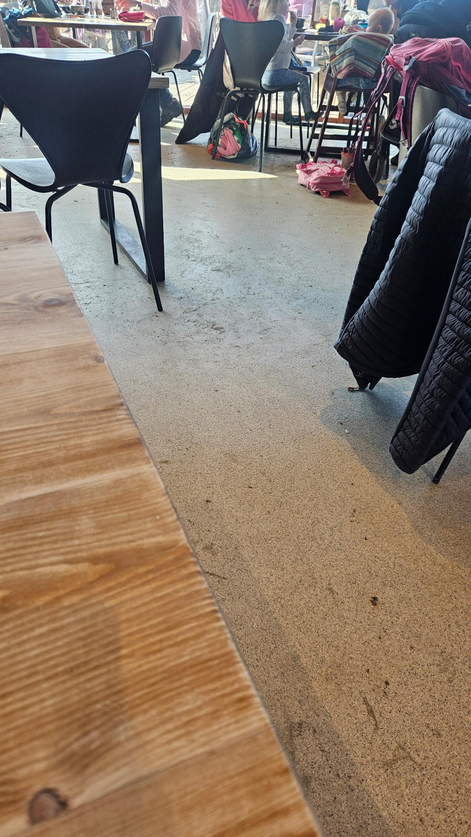 Table in foreground left. Chairs and tables in centre. Coats on chairs right.