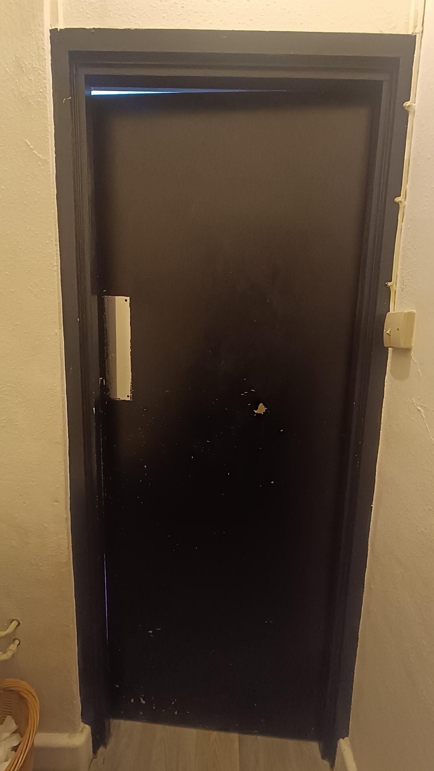 From door facing straight. Black metal toilet door ahead. Push from handle on left to open.