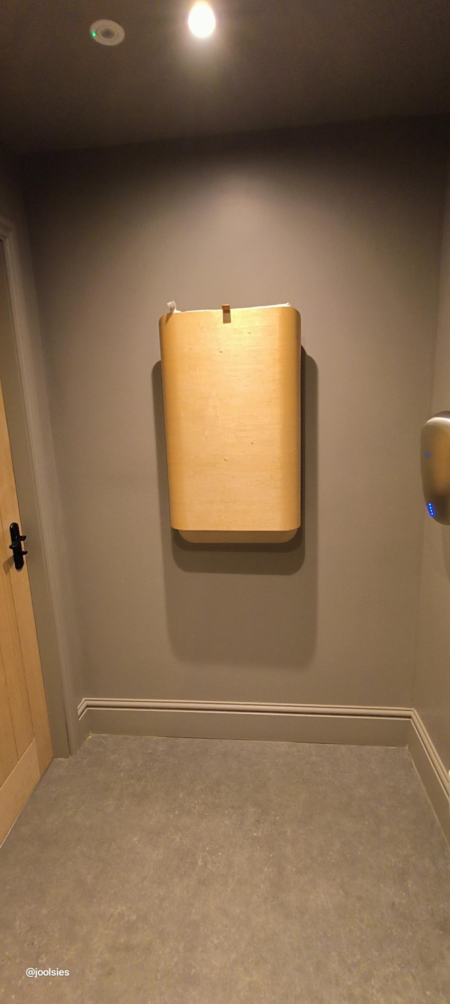 Baby changing station on back wall. Door on left wall. Dispenser on right wall.
