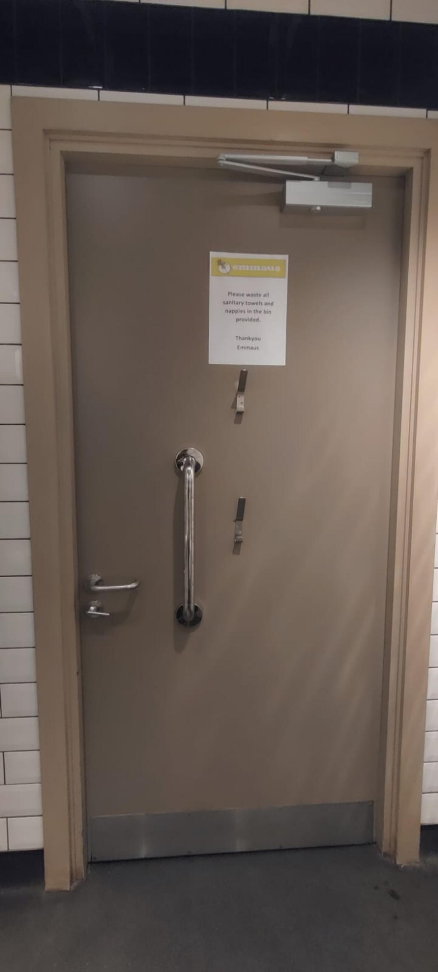 Back of door. Beige door. Silver vertical grabrail in centre. Hooks to its right. Push metal handle on left open.