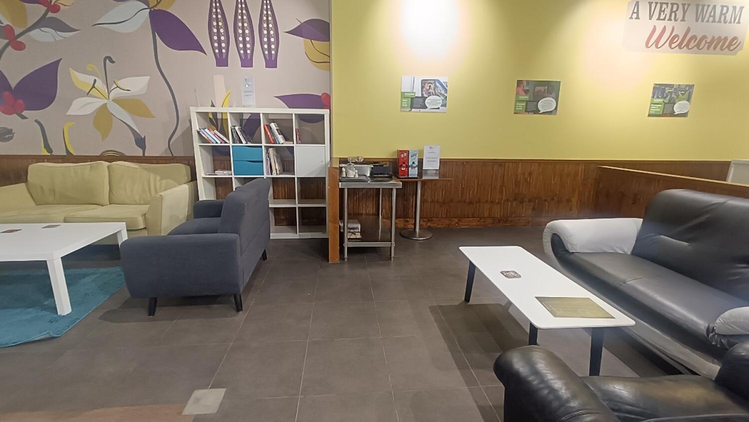 From partition facing straight. Couch and table along back left and right. Condiment station at back centre.