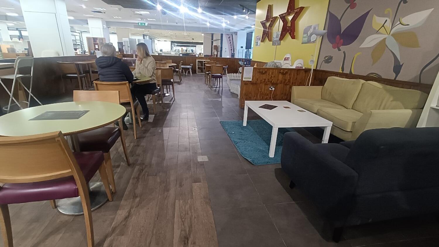 From condiment station facing left. Tables and chairs along left. Couch and table on right. Second partition behind it.