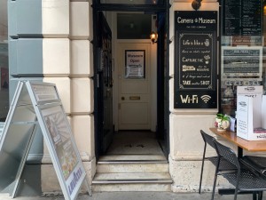 From street, facing entrance. Outdoor seating to right of path. Path straight to entrance door ahead. Sign on left of path.