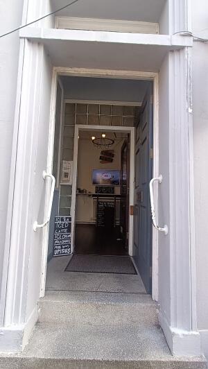 Grey wood-panelled door to venue. Push from handle on left to open. Handrail on both sides before door.