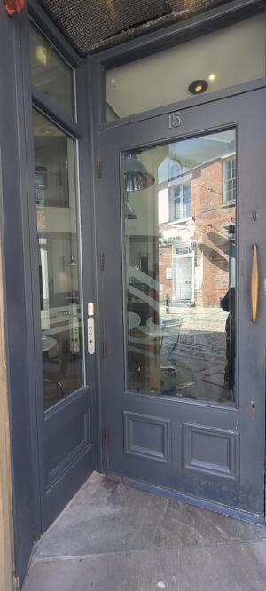 Grey framed metal glass door ahead. Pull metal handle to open on right. Disabled assistance bell on left.