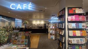 From back left of book shop facing straight. Bookshelves along both sides. Open entrance in centre.
