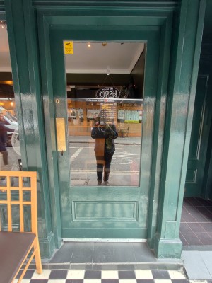 Glass door with green frame ahead. Push golden metal panel on left to open.
