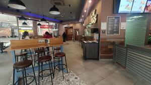 From entrance facing straight. High table with stools along left. Bin at back center. Partition along right.
