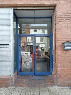 Blue metal-framed glass doors ahead. Pull from red handles at centre to open.