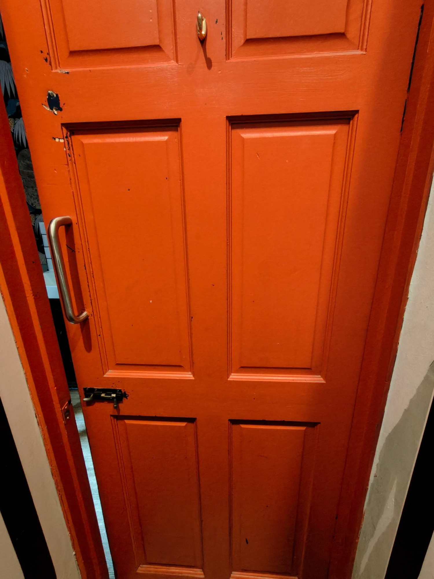 From toilet facing back of toilet door. High hanging hook at top centre. Push silver metal handle on left to open.