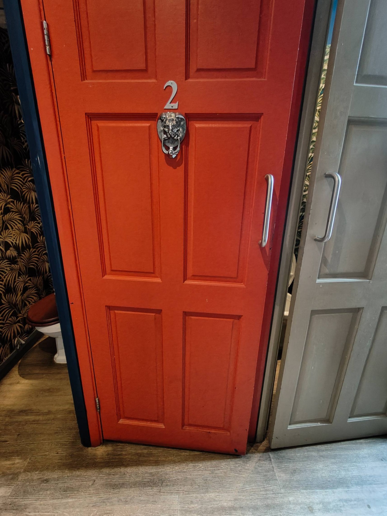 Facing red toilet cubicle door. Pull silver metal handle on right to open.