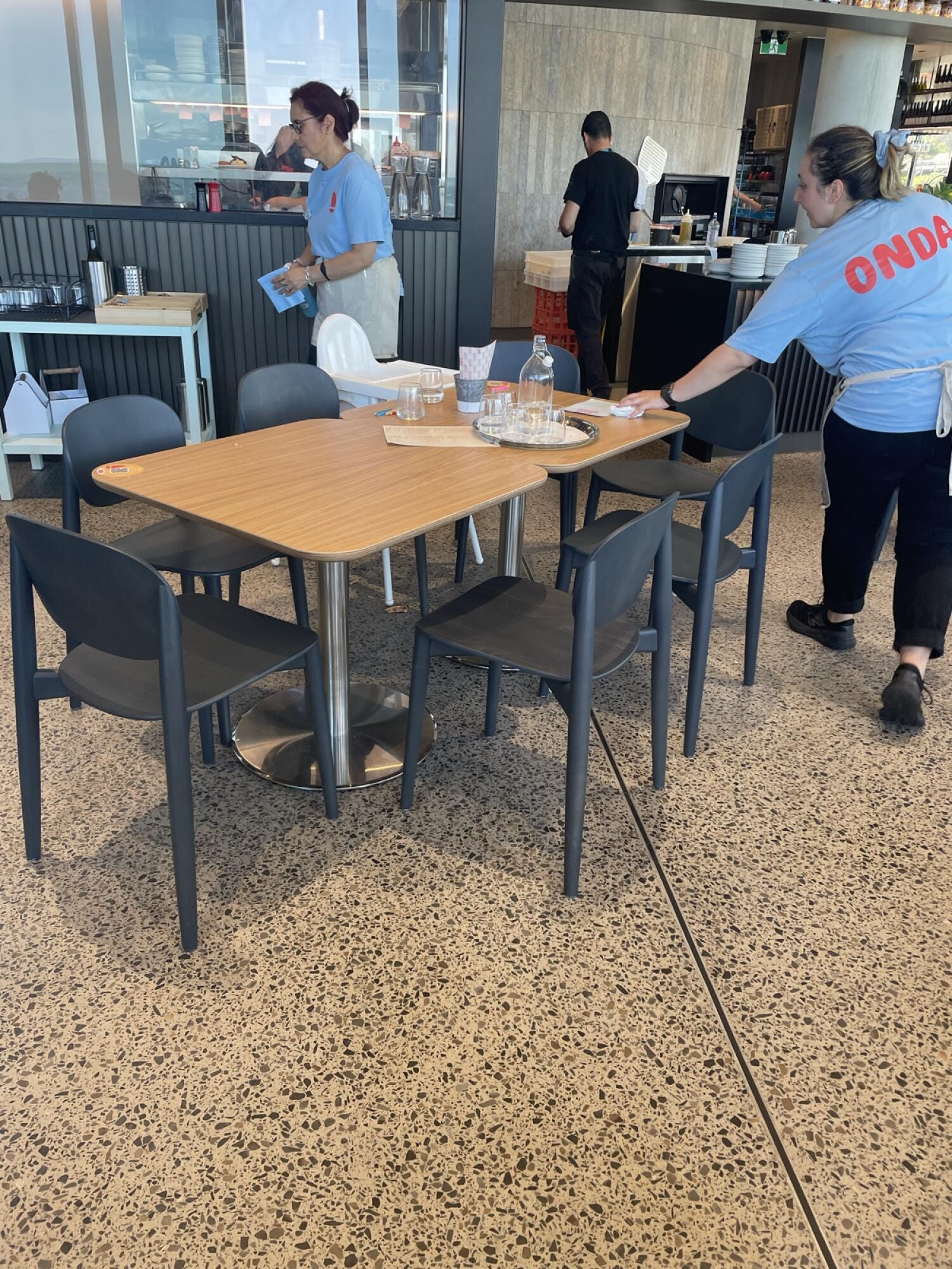 Table with six chairs in centre. Baby high chair behind table. Counter along back wall.