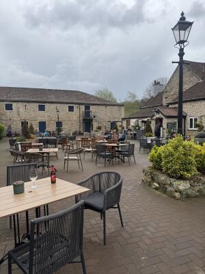 Tables and chairs spaced across courtyard. Bushes on right in stone planter.