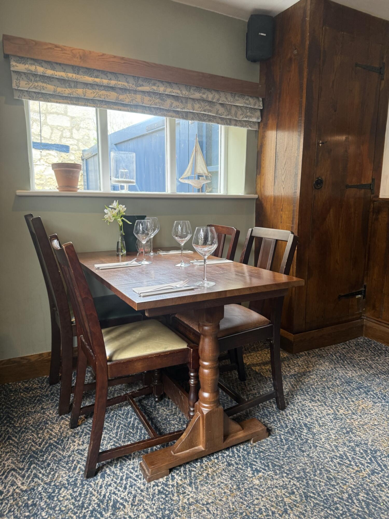 Table with four chairs in centre. Window with blinds behind.
