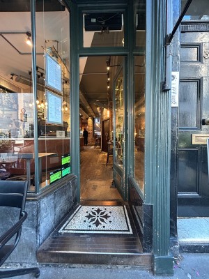 Archway and step up to single glass door with dark green frame. Vertical gold handle left, push to open.