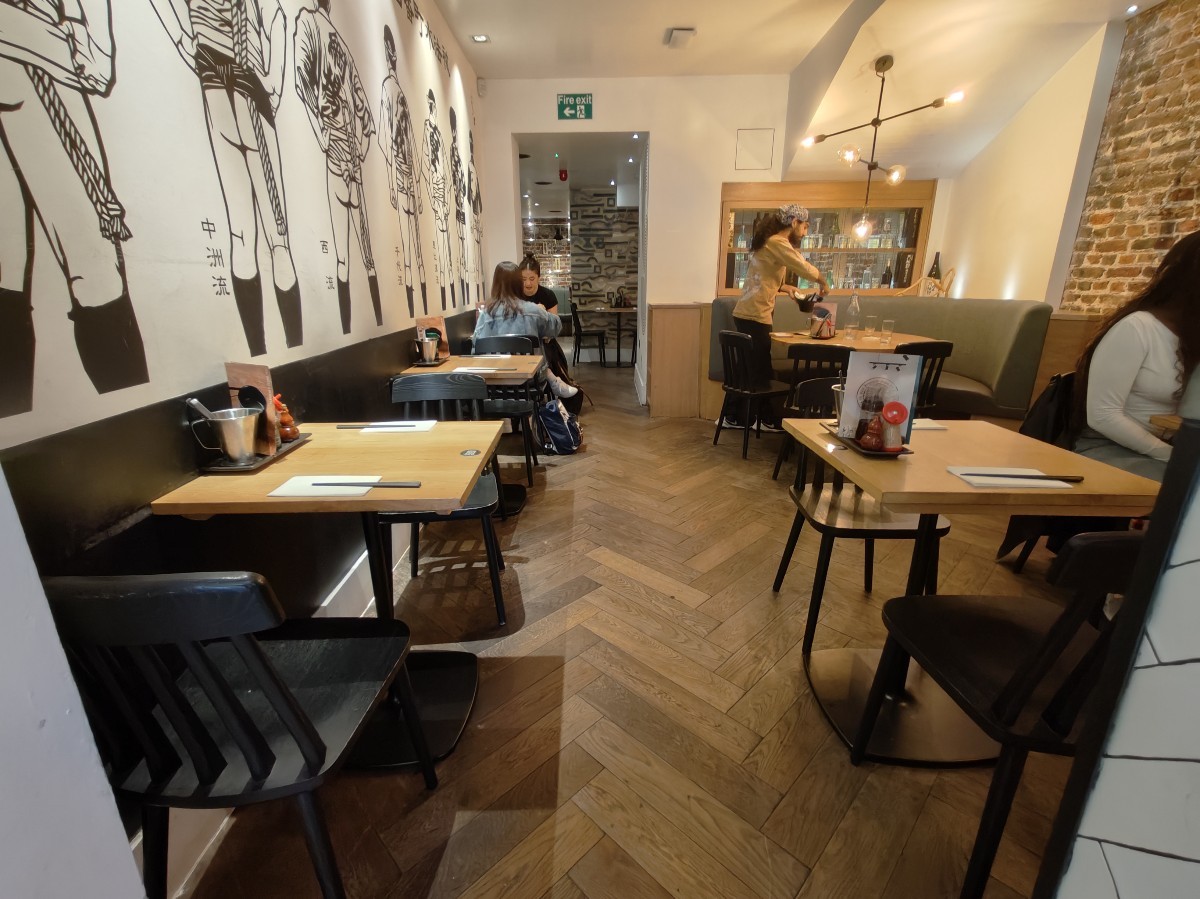 From end of bar facing straight. Tables and chairs along left. Straight path to archway to back area. Table and chairs on right.