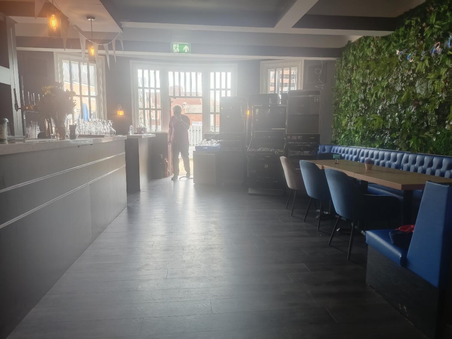 From end of path facing left. Bar counter along left. Booth seating, tables and chairs along right.