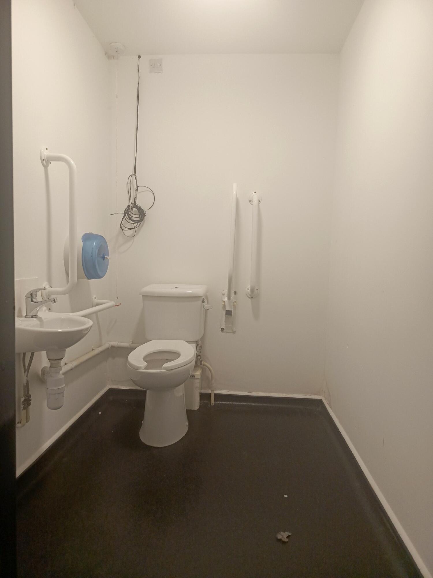 From door facing straight. Sink on left wall. Toilet at back. Emergency pull cord to it's left.