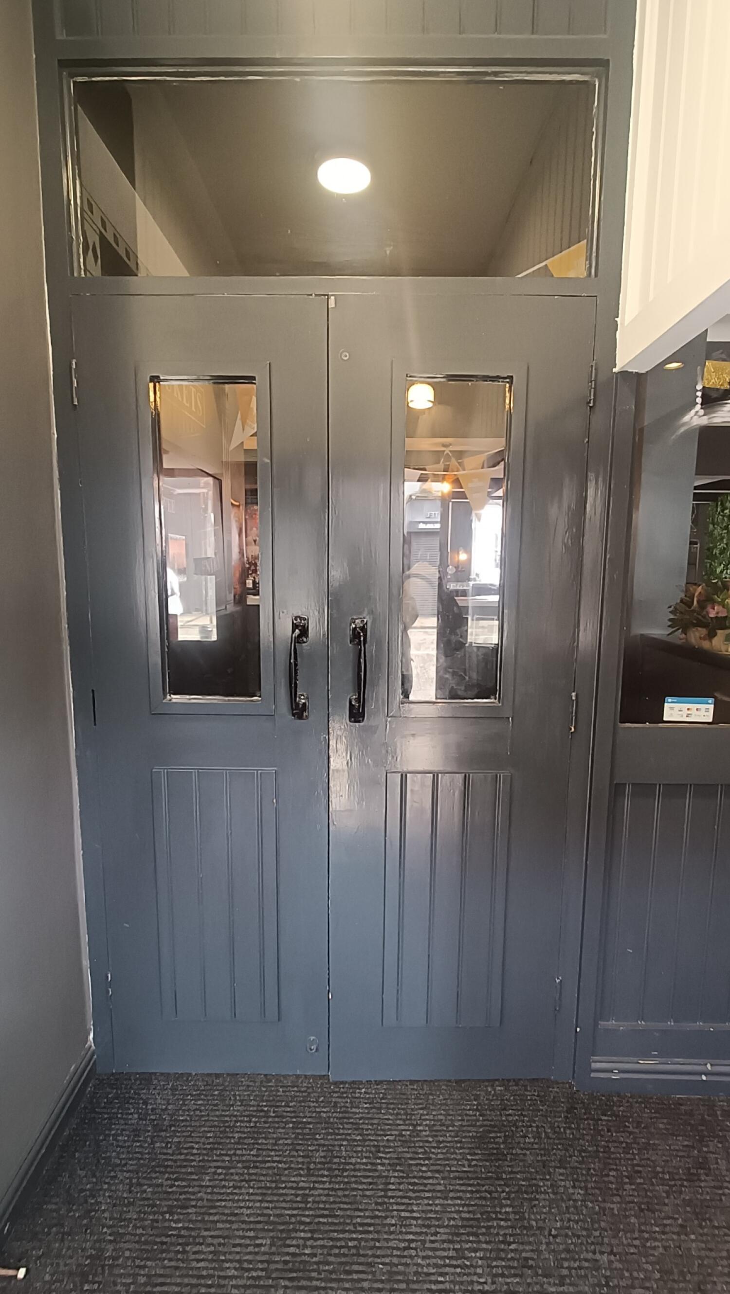 From door facing straight. Dark grey wood-panelled glass door ahead. Pull handles in centre to open.