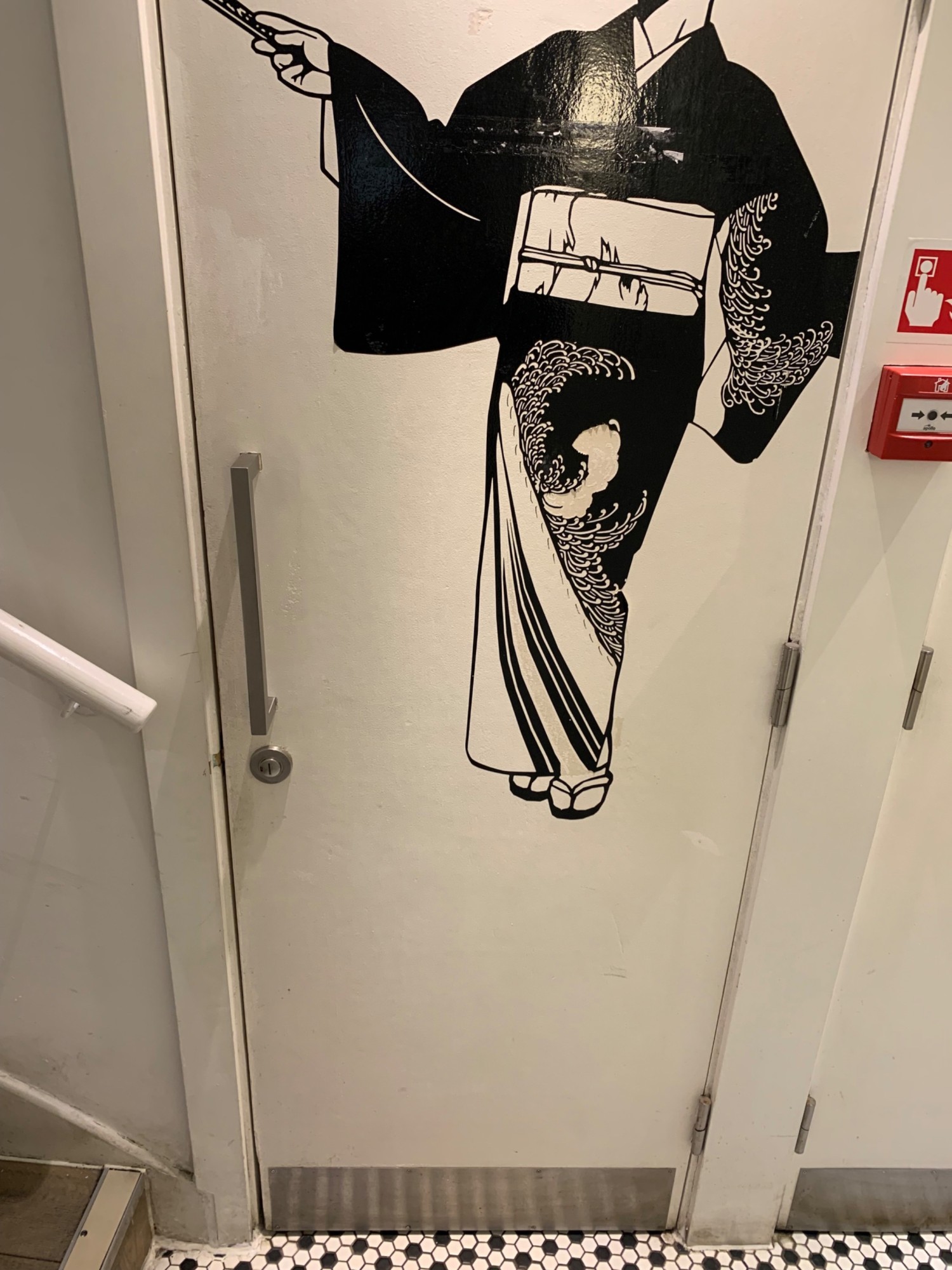 From bottom of stairs, looking left. Toilet door ahead. White door with black graphic. Pull from silver metal handle on left of door to open.
